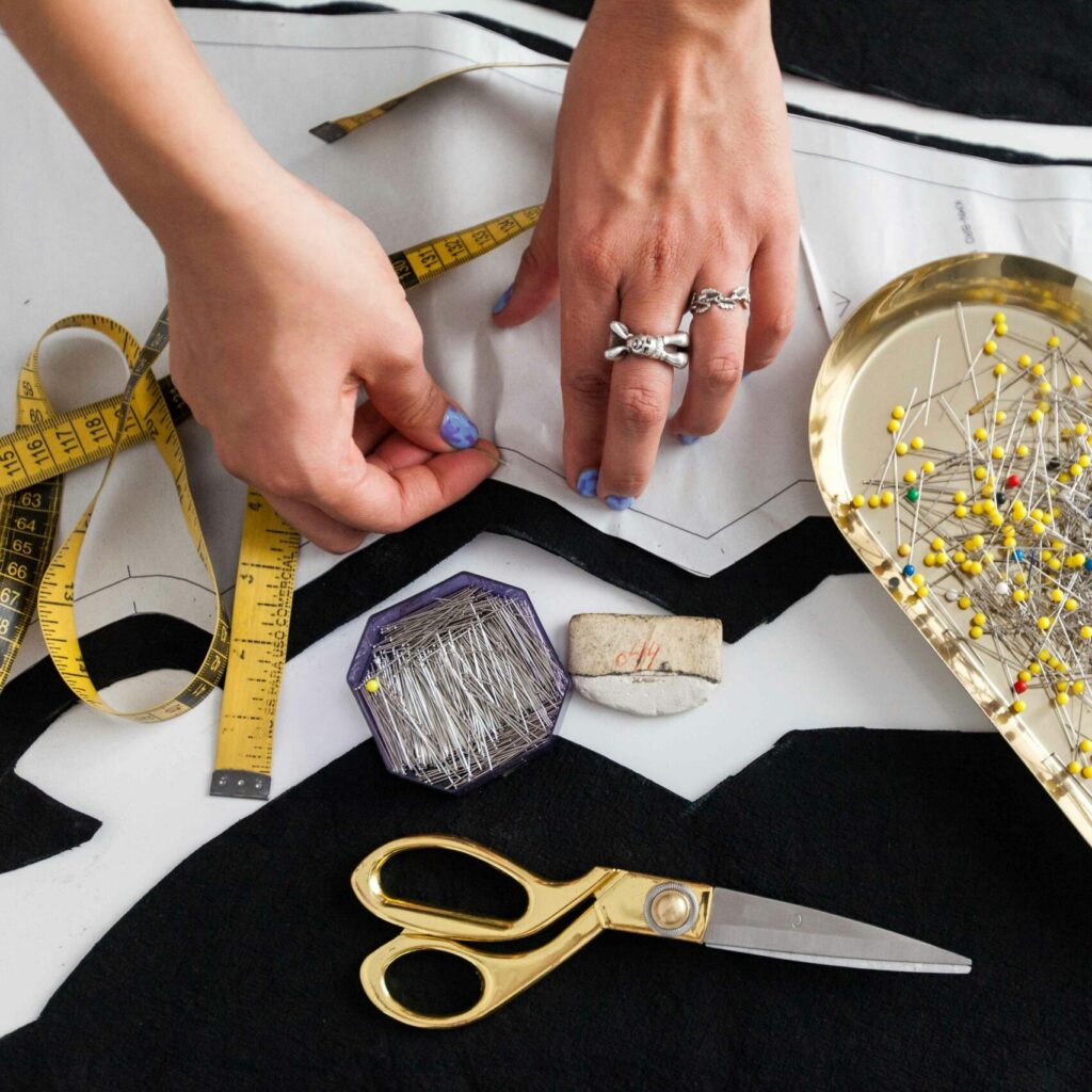 A pair of hands working on garment design with sewing tools on a table.
